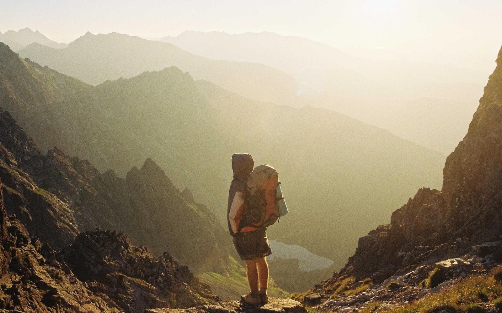 Pessoa com mochila observando um vale nas montanhas ao amanhecer, com neblina leve