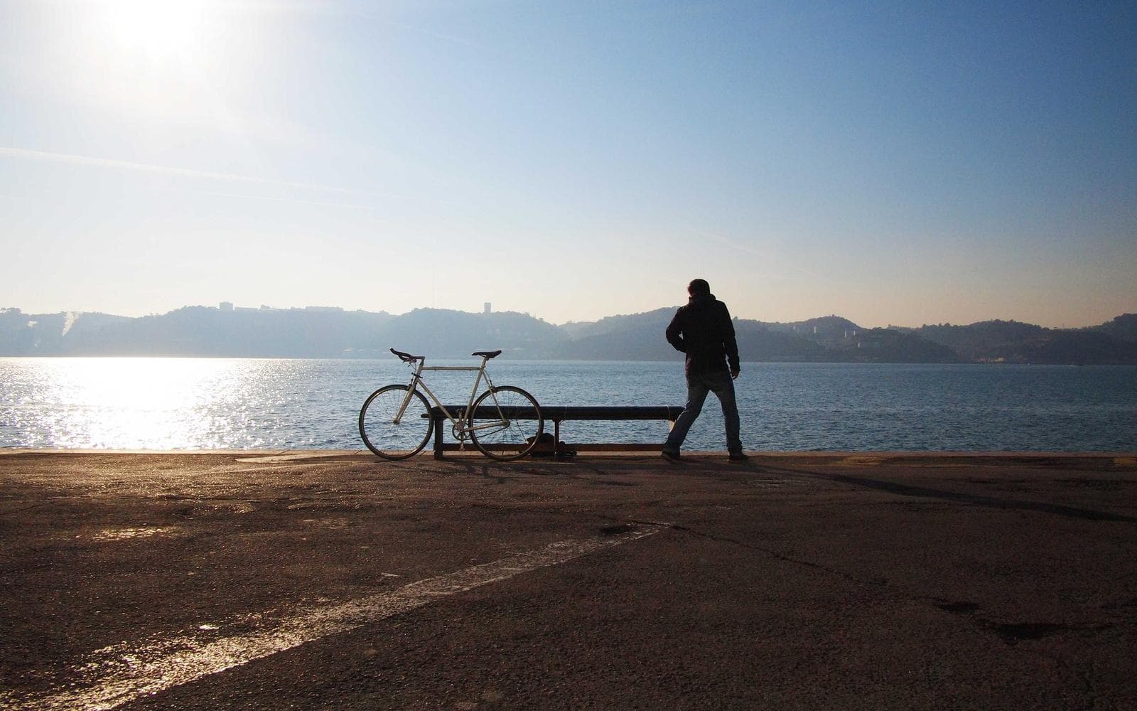 Pessoa parada ao lado de uma bicicleta à beira de um lago, luz do fim de tarde