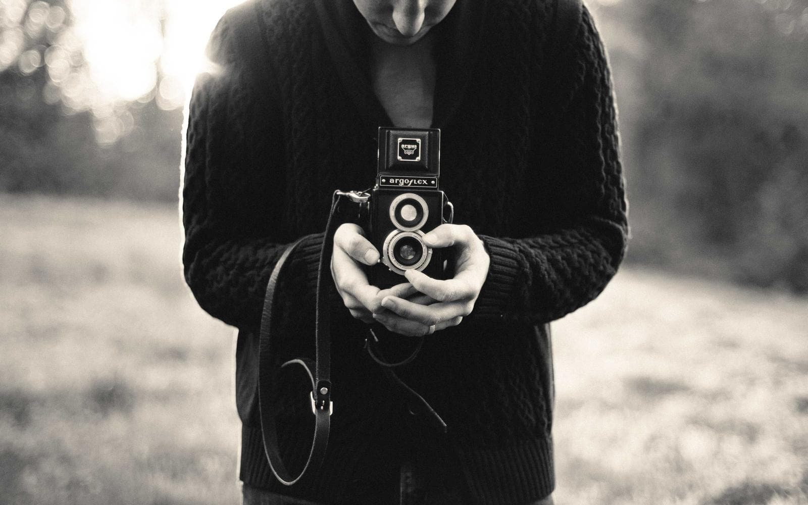 Pessoa segurando uma câmera fotográfica antiga entre as mãos, em preto e branco